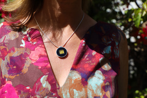 A woman in a pink floral dress wears a black and gold pendant from the RT Signature Collection by Ronnie Taubenfeld