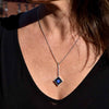 Sterling silver square set with a blue dot of glass in black resin hanging from silver bead chain.