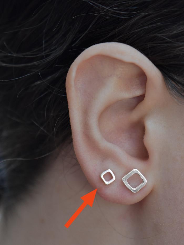 Doyo Studs Earrings Ronnie Taubenfeld shown on a woman's ear marked with a red arrow next to the larger Jingbo studs for scale