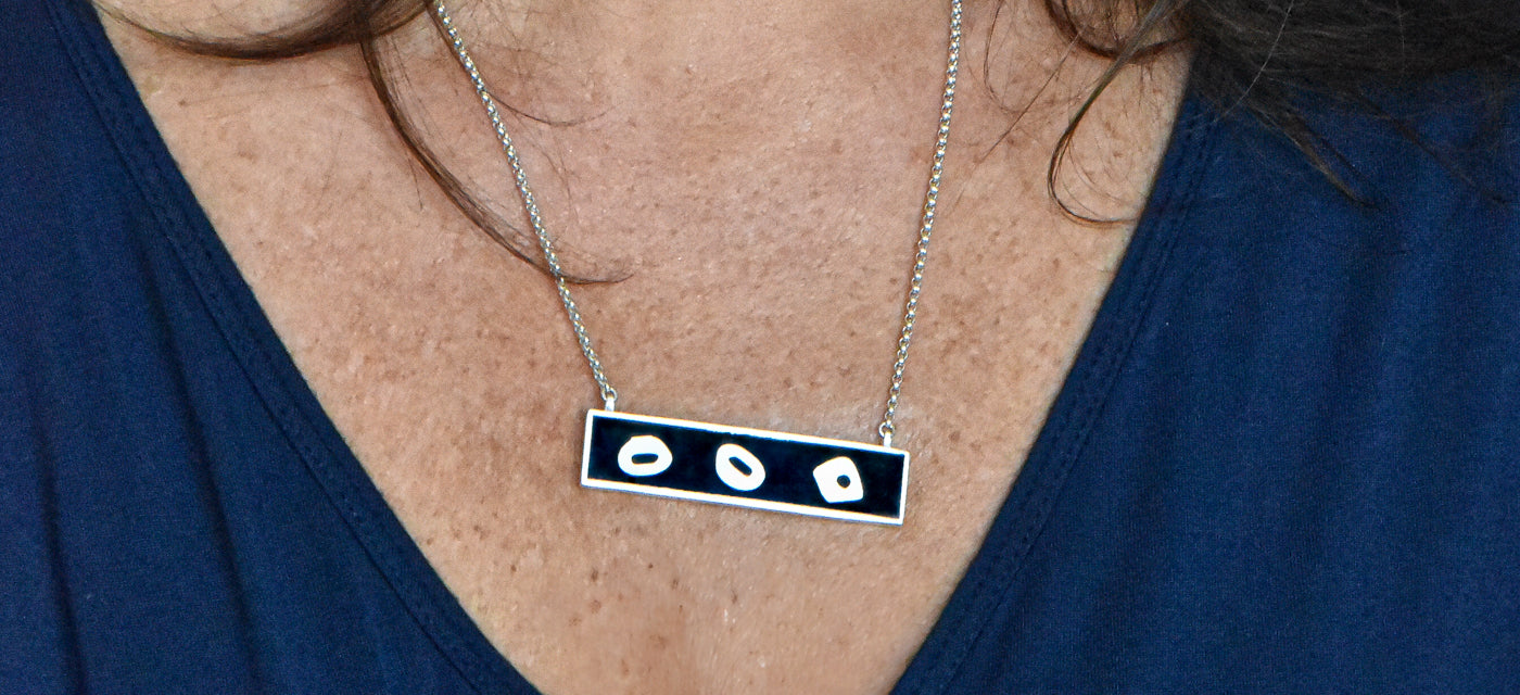 A rectangular silver pendant with abstract silver shapes embedded in black resin hangs from a silver chain.