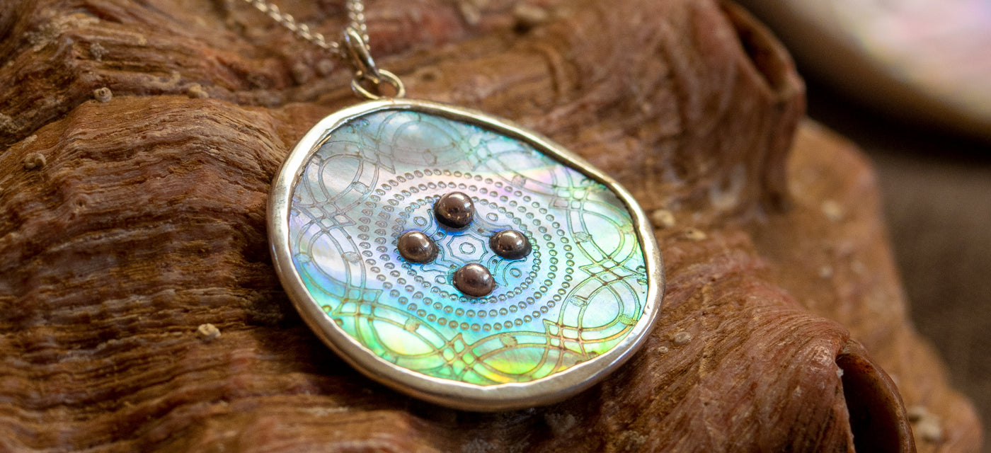 A rainbow hued mother-of-pearl button is set in sterling silver and hangs from a silver chain.