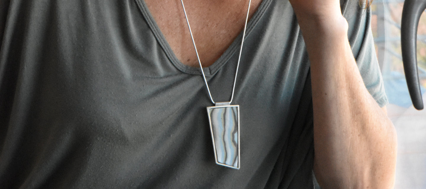 A porcelain handmade tile set in a sterling silver pendant hanging from a silver chain.