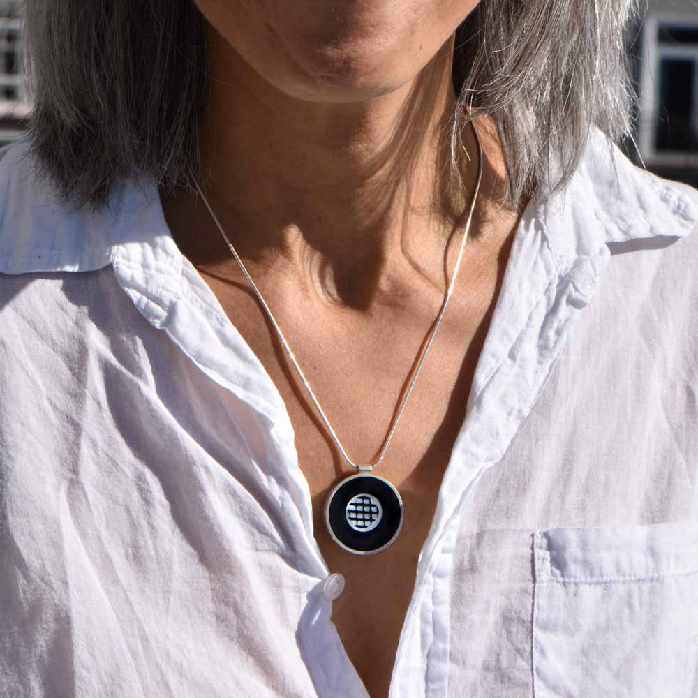Mother of pearl grid set in black resin and framed by a round sterling silver setting, hanging from a sterling silver chain.
