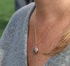 Iridescent carved mother of pearl button necklace set in 14K gold and hanging from 14K gold chain.