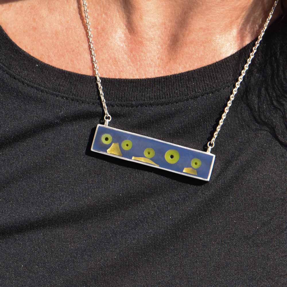 Sterling silver bar pendant with 24K gold-fused glass and green glass embedded in dark gray resin, hanging from a sterling silver chain.