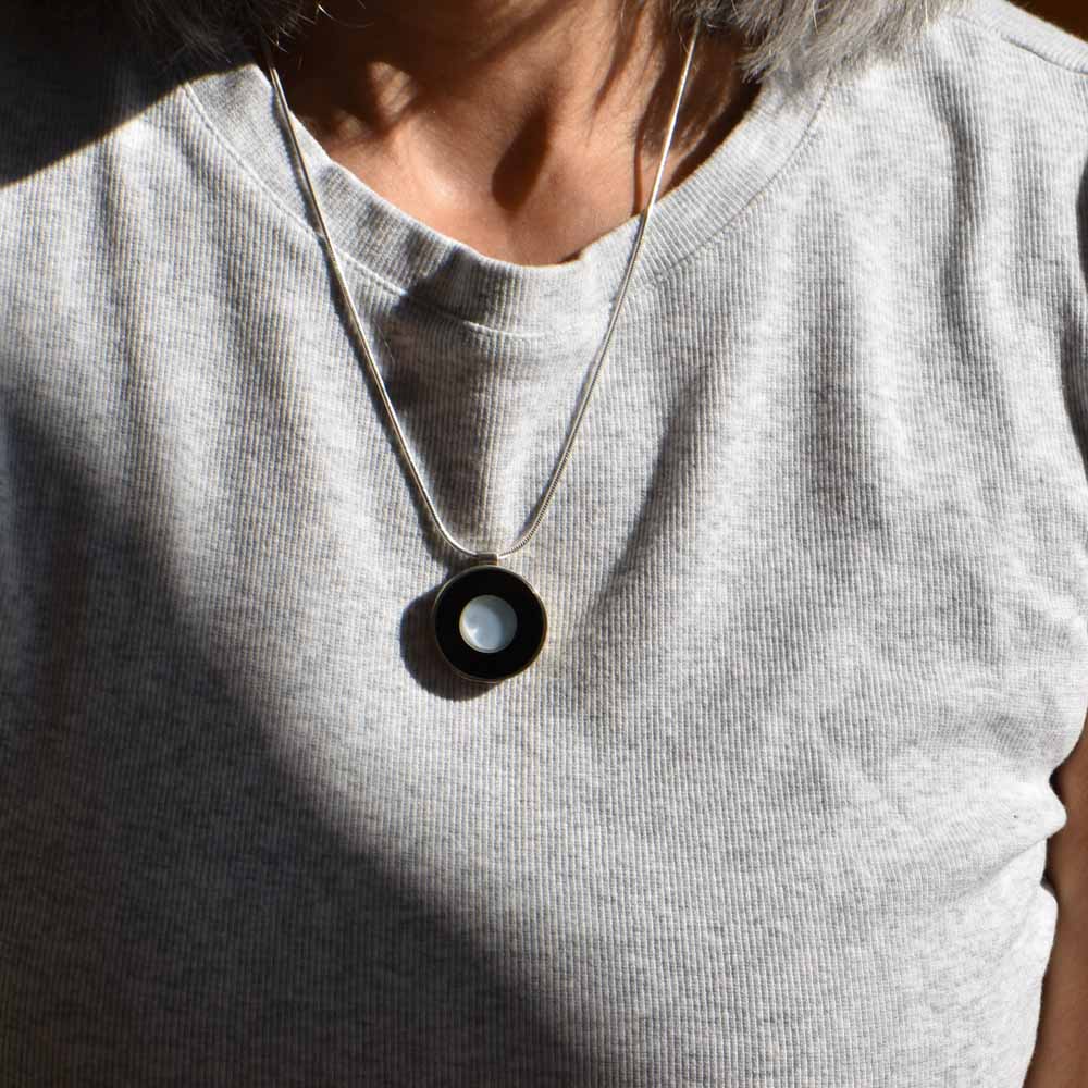 A transparent blue glass disk is set in black resin, framed by a round sterling silver setting and hanging from a silver chain.