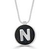 N is For... Necklace by Ronnie Taubenfeld is a handmade circular sterling silver setting showcasing a white porcelain letter N embedded in black resin. Suspended from a silver snake chain.