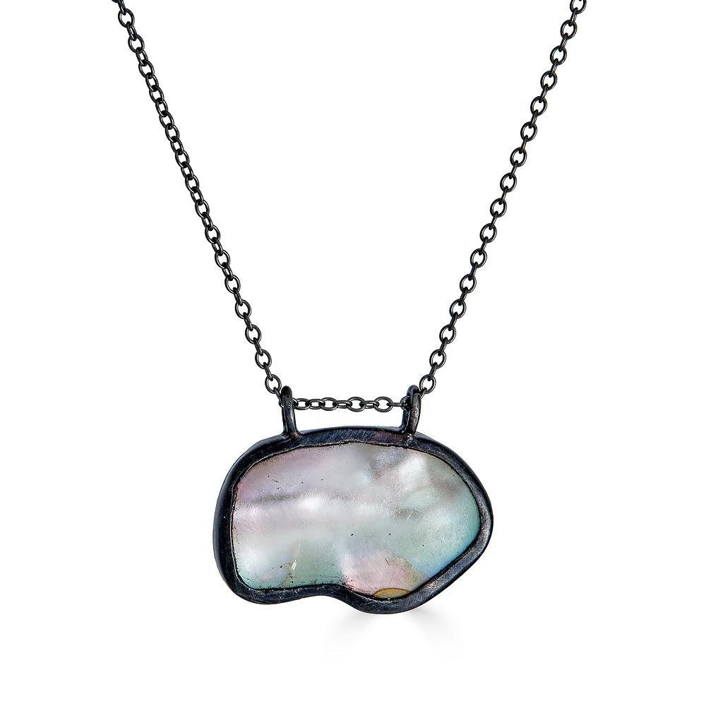 Reflection Necklace by Ronnie Taubenfeld is an iridescent mother of pearl shape hand set in oxidized sterling silver hanging from a black silver cable chain.