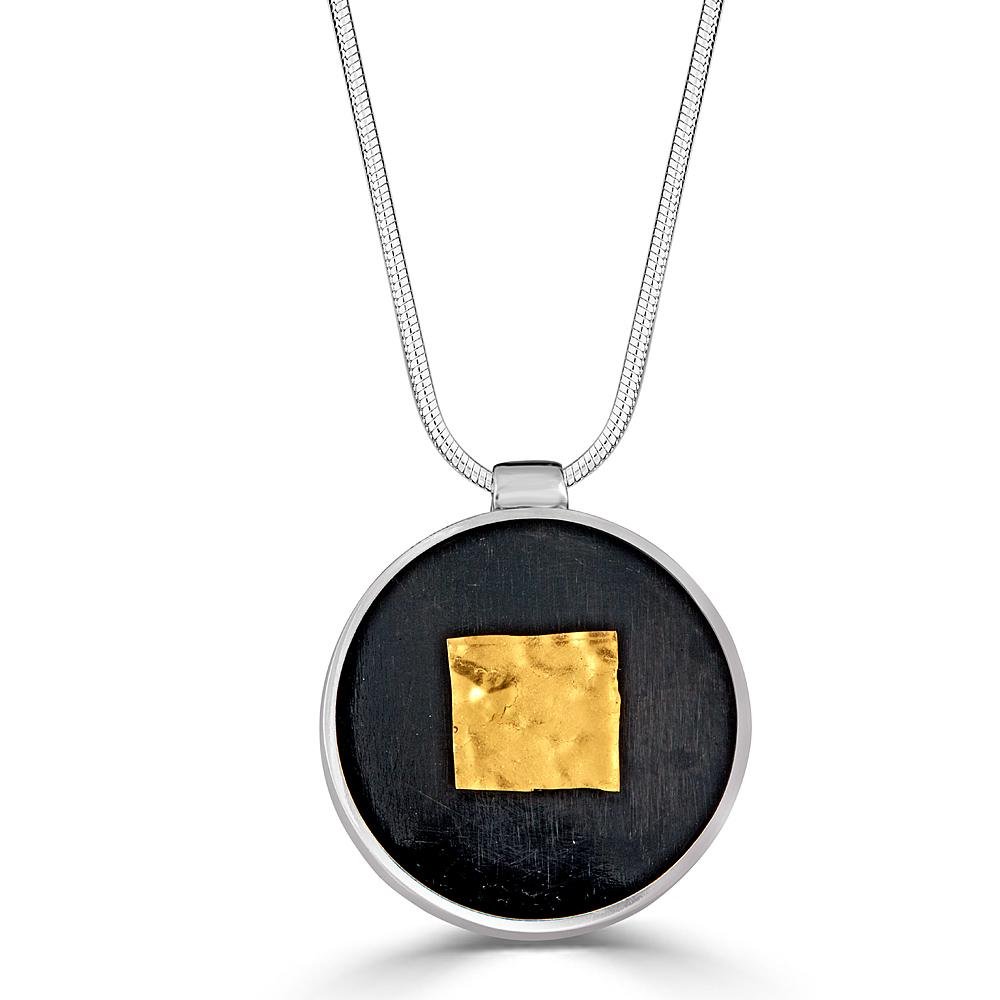 Square Shimmer Necklace Necklace by Ronnie Taubenfeld is a yellow gold-fused glass square embedded in black resin and set in a circular silver frame, suspended from a silver snake chain.