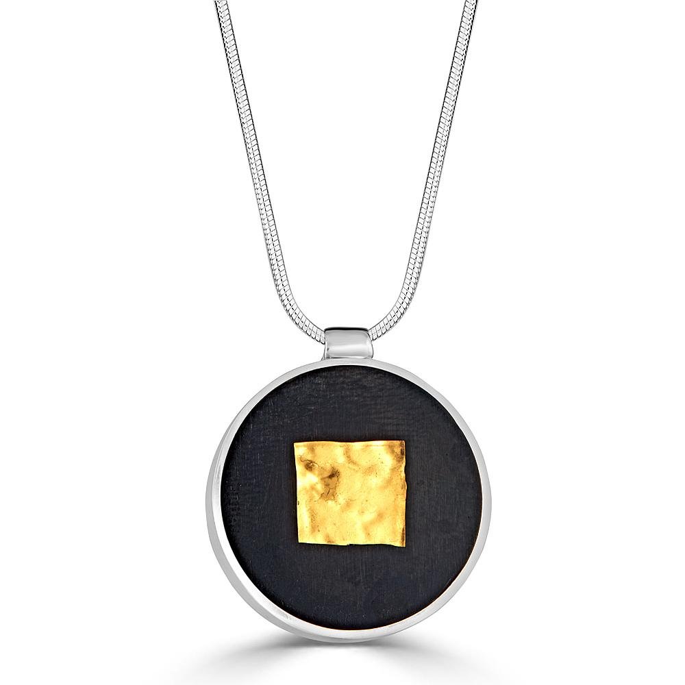 Square Shimmer Necklace by Ronnie Taubenfeld is a yellow gold-fused glass square embedded in black resin and set in a circular silver frame, suspended from a silver snake chain.