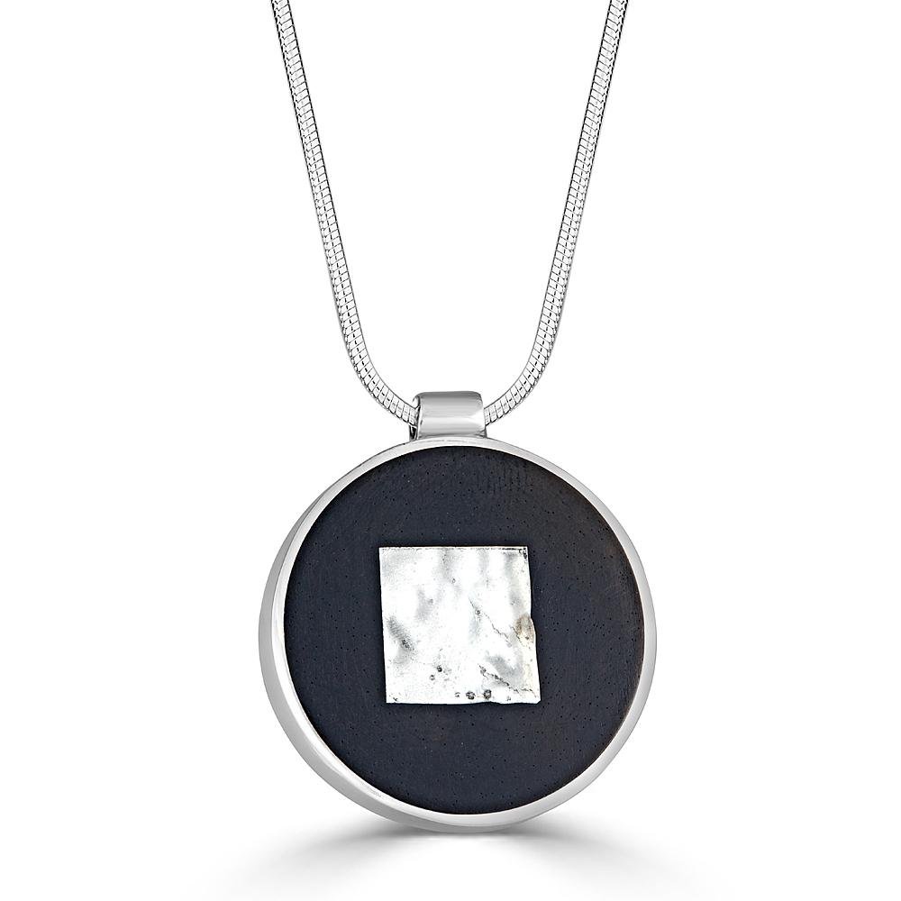 Square Shimmer Necklace Necklace by Ronnie Taubenfeld is a white gold-fused glass square embedded in black resin and set in a circular silver frame, suspended from a silver snake chain.