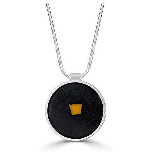 Tiny Fragment Necklace by Ronnie Taubenfeld is a tiny yellow square of Murano glass embedded in black resin and set in a circular sterling silver frame, hanging from a silver snake chain.