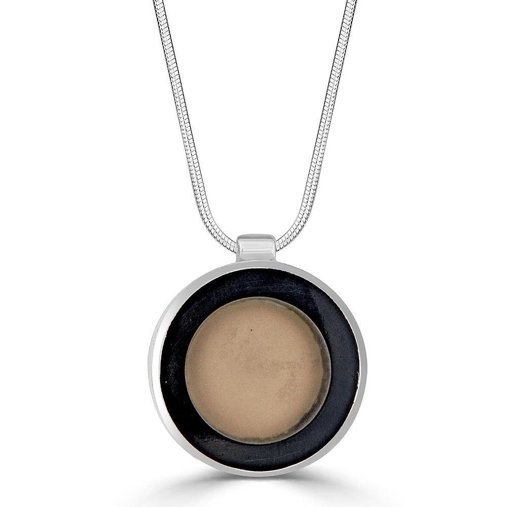 Transparent Beauty Necklace by Ronnie Taubenfeld is a transparent glass disk with a beige backing embedded in black resin and set in a circular silver frame, suspended by a silver snake chain.