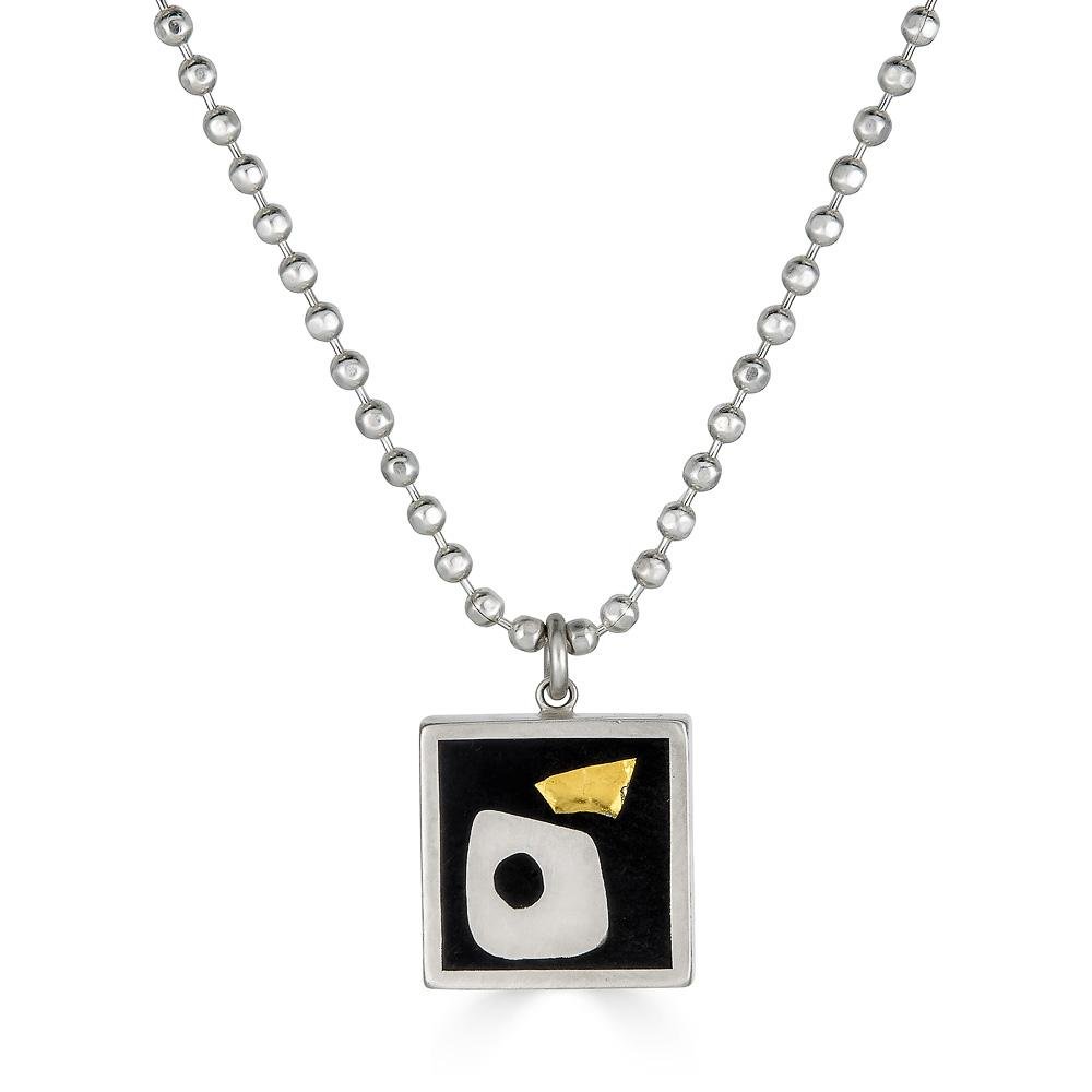 Under & Over Pendant by Ronnie Taubenfeld is handmade with 24K yellow gold-fused Murano glass  and a modern silver shape embedded in black resin and set in a square sterling silver frame, hanging from a silver ball chain.