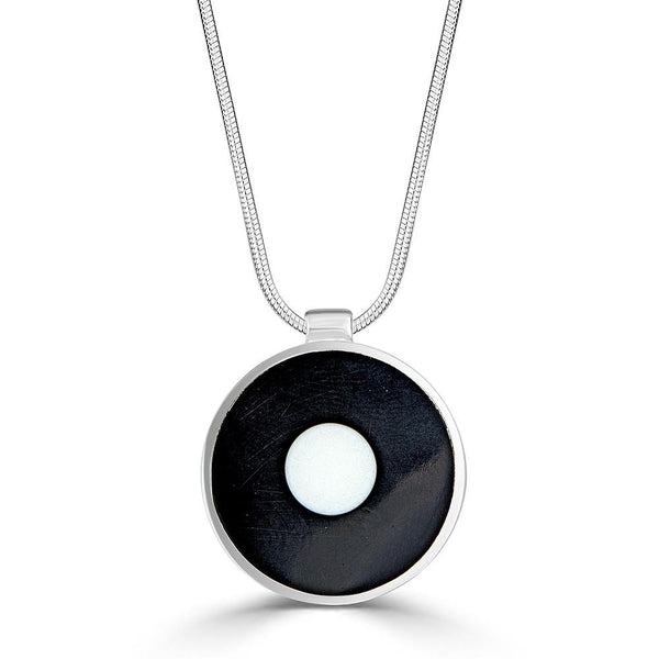 White Disk Necklace by Ronnie Taubenfeld is a white glass circle embedded in black resin, framed by a circular silver setting and hanging from a silver snake chain.